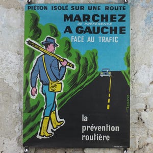 Può includere: Poster vintage francese sulla sicurezza stradale. Il poster mostra una persona che cammina sul lato sinistro della strada, di fronte al traffico. Il testo francese recita "Cammina a sinistra, di fronte al traffico". Il poster ha una combinazione di colori blu, verde e nero.