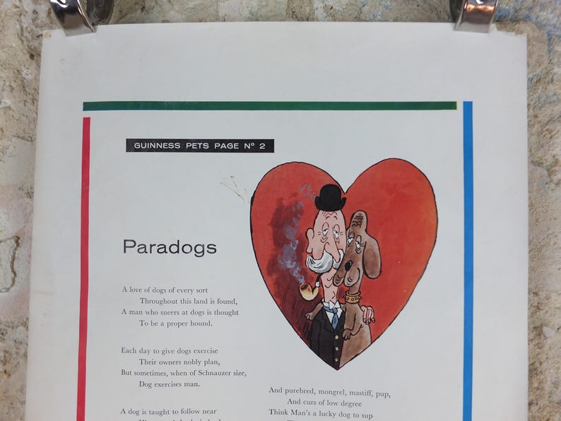 May include: A vintage print from the Guinness Pets series, with a cartoon illustration of a man and a dog inside a red heart. The text reads "Paradogs" and includes a poem about dogs. The print is held by silver clips.