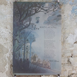 May include: A framed print of "Bilbo's Last Song" by J.R.R. Tolkien. The artwork features a landscape with trees, a boat, and a town, rendered in shades of blue and green. The poem's text is displayed on the left side.