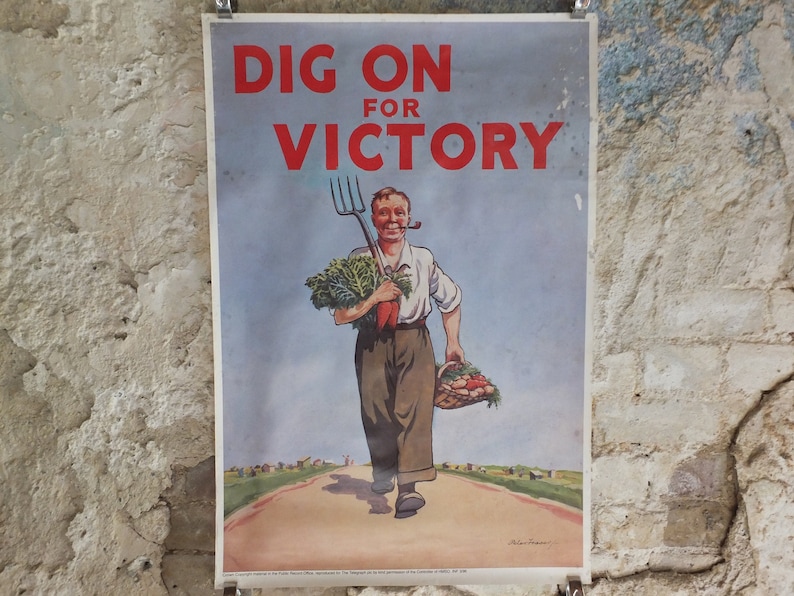 Puede incluir: Cartel vintage con el texto "DIG ON FOR VICTORY" en rojo. Muestra a un hombre con pipa, llevando un horca, zanahorias y una cesta de verduras. El cartel est&aacute; montado en una pared texturizada.