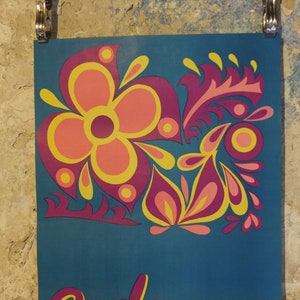 Pu&ograve; includere: Un poster turchese con un design floreale in rosa, giallo e viola. Il design presenta un grande fiore e foglie stilizzate. Il poster &egrave; tenuto da clip argentate contro un muro strutturato.