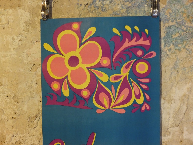 Pu&ograve; includere: Un poster turchese con un design floreale in rosa, giallo e viola. Il design presenta un grande fiore e foglie stilizzate. Il poster &egrave; tenuto da clip argentate contro un muro strutturato.