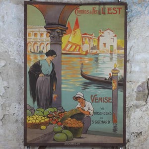 May include: Vintage travel poster for Chemins de Fer de l'Est, featuring a Venetian scene with a gondola, sailboats, and figures near a fruit stand. The poster has text in French and is framed with a brown border.
