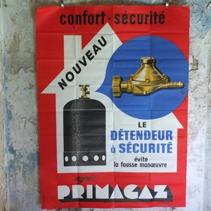 May include: Vintage poster in red, white, and blue. It features a gas cylinder and regulator illustration, with French text including "confort sécurité" and "PRIMAGAZ". The poster is mounted on a textured wall, showing signs of age.