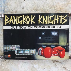 以下が含まれることがあります： コモドール64の「バンコクナイツ」のヴィンテージ広告。ポスターは、ボクシンググローブとボクシングリングのグラフィックを備えた黒い背景が特徴です。「OUT NOW」のテキストが表示されます。