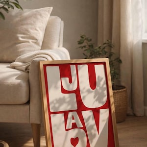 Könnte beinhalten: Ein gerahmter Kunstdruck mit dem Wort "LUV" in großen weißen Buchstaben auf rotem Hintergrund. Der Holzrahmen steht auf einem Holzboden, mit einem neutralfarbenen Sofa und Pflanzen im Hintergrund. Das Herz im "V" fügt eine romantische Note hinzu.