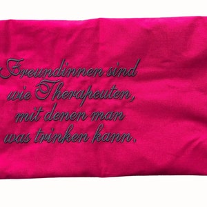 May include: A pink rectangular pillow with black embroidered text that reads "Freundinnen sind wie Therapeuten, mit denen man was trinken kann."