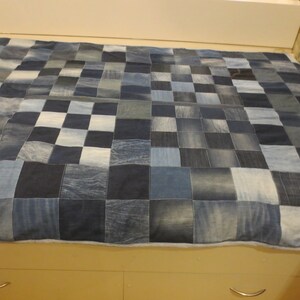 Könnte beinhalten: Eine Patchwork-Decke aus blauen Jeansquadraten. Die Decke liegt auf einem Bettgestell mit zwei Schubladen.