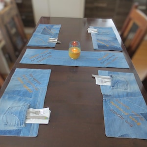 Könnte beinhalten: Ein Holztisch mit vier Platzsets aus Jeans, jedes mit einem anderen Design. Die Platzsets haben bestickten Text und eine Tasche. Eine brennende Kerze steht in der Mitte des Tisches.