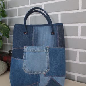 Könnte beinhalten: Eine blaue Jeans-Tragetasche aus recycelten Jeans. Die Tasche hat ein Patchwork-Design mit verschiedenen Blautönen von Jeans und eine große Tasche auf der Vorderseite.