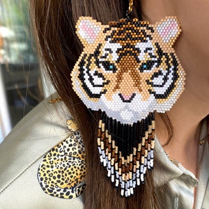 May include: Beaded tiger face earrings with a long fringe of black, white, brown, and gold beads.