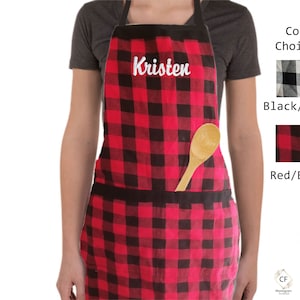 May include: Red and black buffalo check apron with a large pocket and a wooden spoon in the pocket. The apron is personalised with the name "Kristen" in white embroidery.