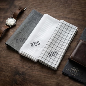 Puede incluir: Tres pa&ntilde;uelos personalizados con las iniciales "RBS" bordadas. Uno es a cuadros grises, otro blanco con rayas y el otro blanco con un patr&oacute;n de cuadr&iacute;cula negra. Tambi&eacute;n hay un reloj y una cartera de cuero marr&oacute;n.