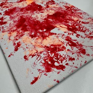May include: Abstract painting on canvas with red and orange paint splatters on a white background.