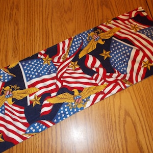 May include: A long rectangular fabric table runner with a blue background and a repeating pattern of American flags, stars, and golden eagles.