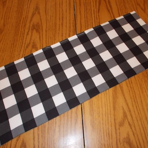 May include: Black and white checkered table runner with a gray background. The runner is folded in half and is lying on a wooden surface.