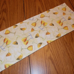 May include: Rectangular beige placemat with a repeating pattern of wine glasses filled with amber liquid. The glasses are in various orientations, with stems and bases in white and gray.