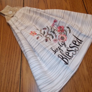 May include: White kitchen towel with brown stripes and a floral design. The towel has a brown loop for hanging and the text "simply blessed" printed on it.