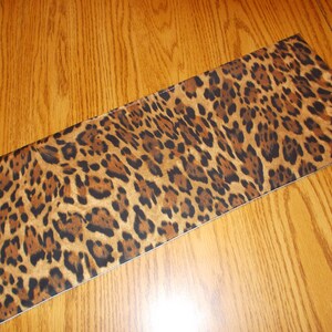 May include: A brown and black leopard print table runner. The runner is made of a soft, fabric material and has a smooth, flat surface.