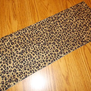 May include: A brown and black leopard print fabric with a subtle textured surface.