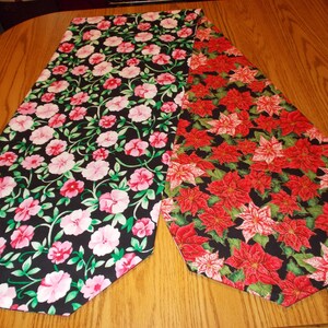 May include: Two decorative table runners. One features pink and red flowers with green vines on a black background. The other has red poinsettias with green leaves on a black background. Both are on a wooden table.