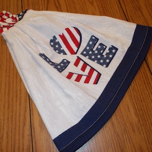 May include: A white tea towel with a blue trim and a red, white, and blue "LOVE" design in the shape of a heart.