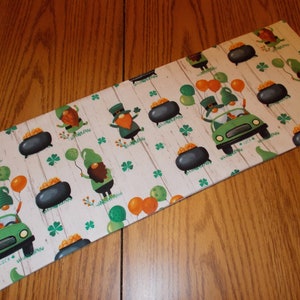May include: Rectangular St. Patrick's Day themed placemat featuring a repeating pattern of green gnomes, pots of gold, shamrocks, and balloons on a white wood-grain background. A green car with gnomes is also featured.