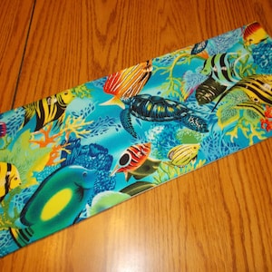 May include: A blue fabric with a colorful tropical fish and coral reef pattern. The fabric features a variety of fish, including angelfish, butterflyfish, and a sea turtle.