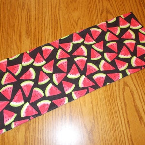 May include: Black fabric with a repeating pattern of red watermelon slices on a black background.