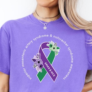 May include: Purple t-shirt with a green and purple ribbon with flowers and the text "Superior mesenteric artery syndrome & nutcracker syndrome awareness SMAS & NCS".