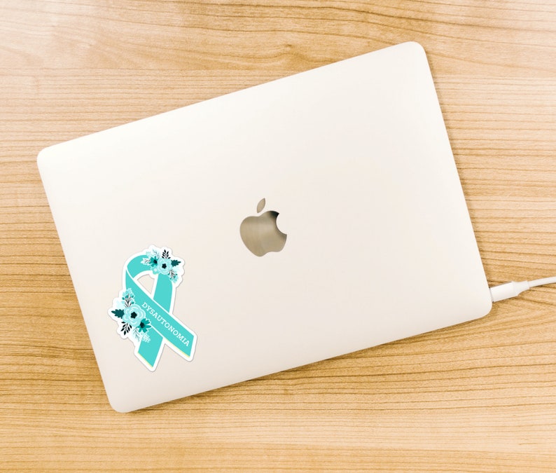 Op de afbeelding: Een turquoise lint met witte bloemen en het woord "DYSAUTONOMIA" op een witte laptop.