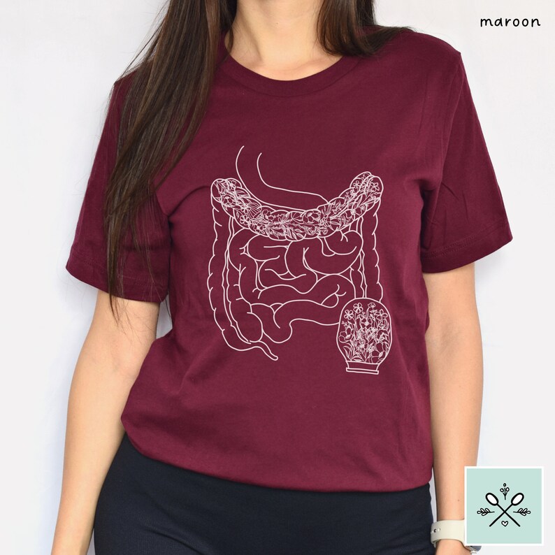 May include: A maroon t-shirt with a white outline of the human digestive system, including the small and large intestines, and a light bulb with flowers inside.