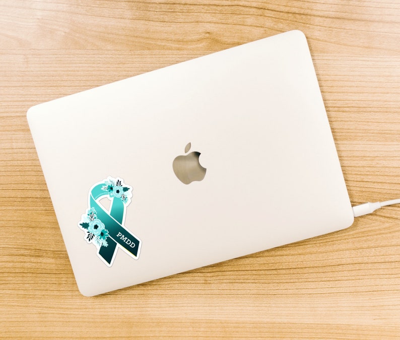 May include: A teal blue ribbon with white flowers and the text "PMDD" on a white laptop.