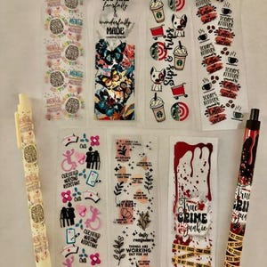 Könnte beinhalten: Eine Sammlung von zehn transparenten Lesezeichen mit verschiedenen Designs. Die Lesezeichen zeigen Bilder von Schmetterlingen, Kaffeetassen, einem Hund, einem Gehirn, einer Krankenschwester, einem Kreuz und einem Tatort. Die Lesezeichen sind alle auf weißem Hintergrund.