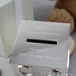 May include: Silver-colored piggy bank shaped like alphabet blocks with a slot for coins. The bank is engraved with the text "Willow Grace", "On Your Christening Day", "29th August 2021", and "All My Love Auntie Marie xxx".