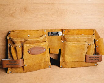 May include: A tan suede tool belt with multiple pockets, metal rivets, and a central metal clip. The belt features two leather loops with the text "Happy Retirement" and "From Work to DIY King" embossed on them. The text "Personalise both Belt Loops" is visible above the belt.