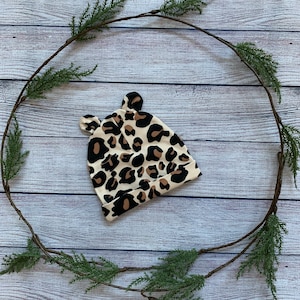May include: A beige and brown leopard print baby hat with ear flaps.