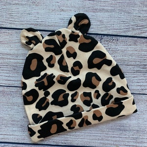May include: A beige and brown leopard print baby hat with ear flaps.