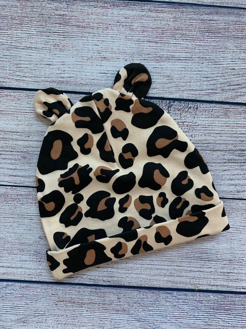 May include: A beige and brown leopard print baby hat with ear flaps.