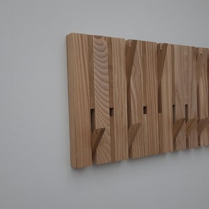 Könnte beinhalten: Ein Wand-Kleiderständer aus Holz mit mehreren Haken. Der Kleiderständer ist aus hellbraunem Holz und hat eine natürliche Oberfläche.
