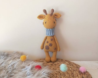 May include: A crocheted giraffe toy with brown spots and a blue scarf. The giraffe is standing on a woven straw mat with a fluffy gray rug in the foreground.