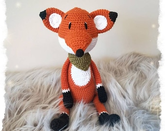 May include: A crocheted orange fox plush toy with white ears and a green scarf. The fox is sitting on a fluffy gray surface.