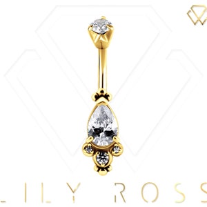 May include: Gold belly button ring with a pear-shaped clear gemstone and smaller clear gemstones on the sides.