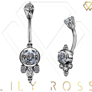 May include: A silver belly button ring with a clear crystal in the center and smaller crystals around it. The ring has a curved bar and a top piece with a single crystal.