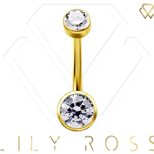 May include: A gold-colored belly button ring with two clear, round, sparkling gemstones. The gemstones are set in a bezel setting. The jewelry has the brand name "LILY ROSS" at the bottom.
