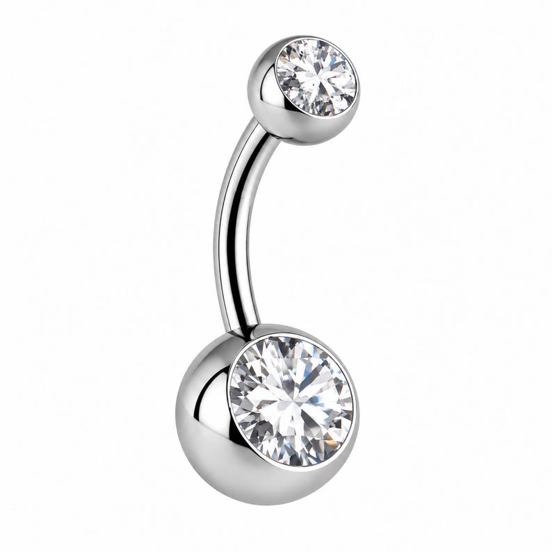 May include: A curved barbell navel ring made of polished silver-toned metal. The piece features two round clear faceted stones set into spherical ends, with a larger stone at the bottom and a smaller stone at the top of the curved bar.