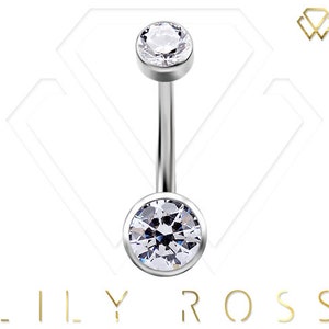 May include: A silver belly button ring with two clear, round, faceted gemstones. The top gem is smaller than the bottom gem. The jewelry is centered on a white background with the brand name "LILY ROSS" in gold lettering.