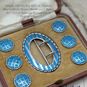 May include: Antique sterling silver and cerulean blue guilloché enamel buckle and six button set. The oval buckle and buttons feature a woven pattern in silver and blue. The set is presented in its original case, with text that reads "Antique 1907 Sterling Silver & Cerulean Blue Guilloché Enamel Buckle and 6 Button Set - Levi & Salaman, Birmingham in Original Case."