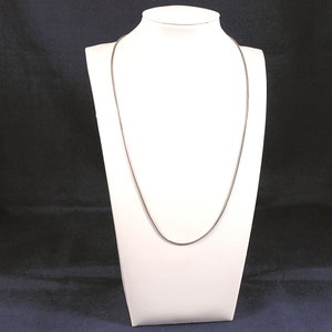 May include: A silver chain necklace displayed on a white mannequin bust.