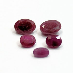 May include: Five oval-shaped gemstones, all a deep reddish-purple color. The stones are of varying sizes, with the largest being about the size of a dime.